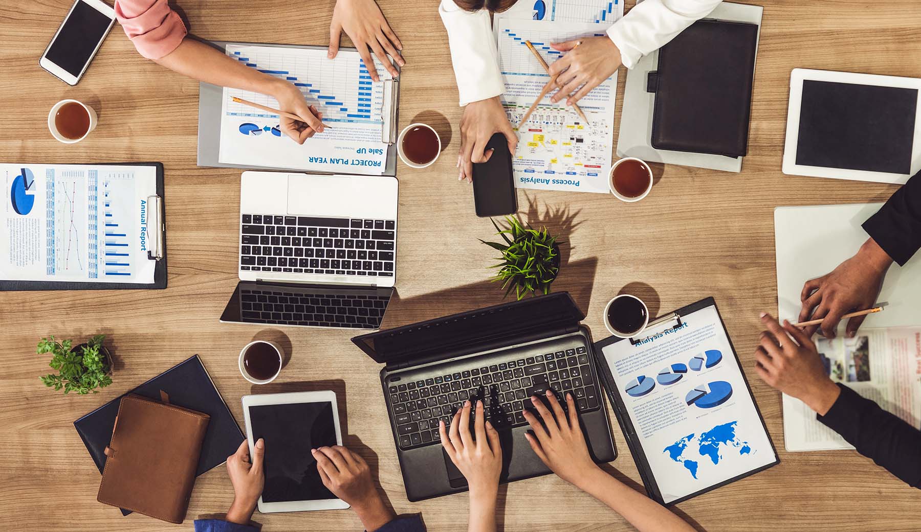 Top view of executives in a group meeting with laptop computer, coffee and documents on a table