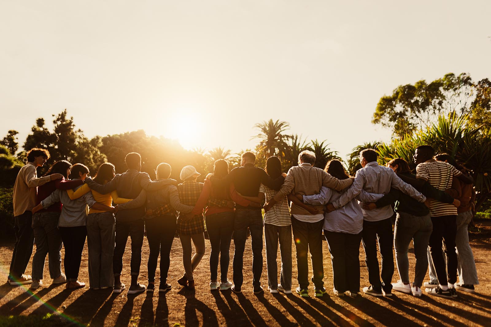Back view of happy multigenerational people embracing in a public park during sunset