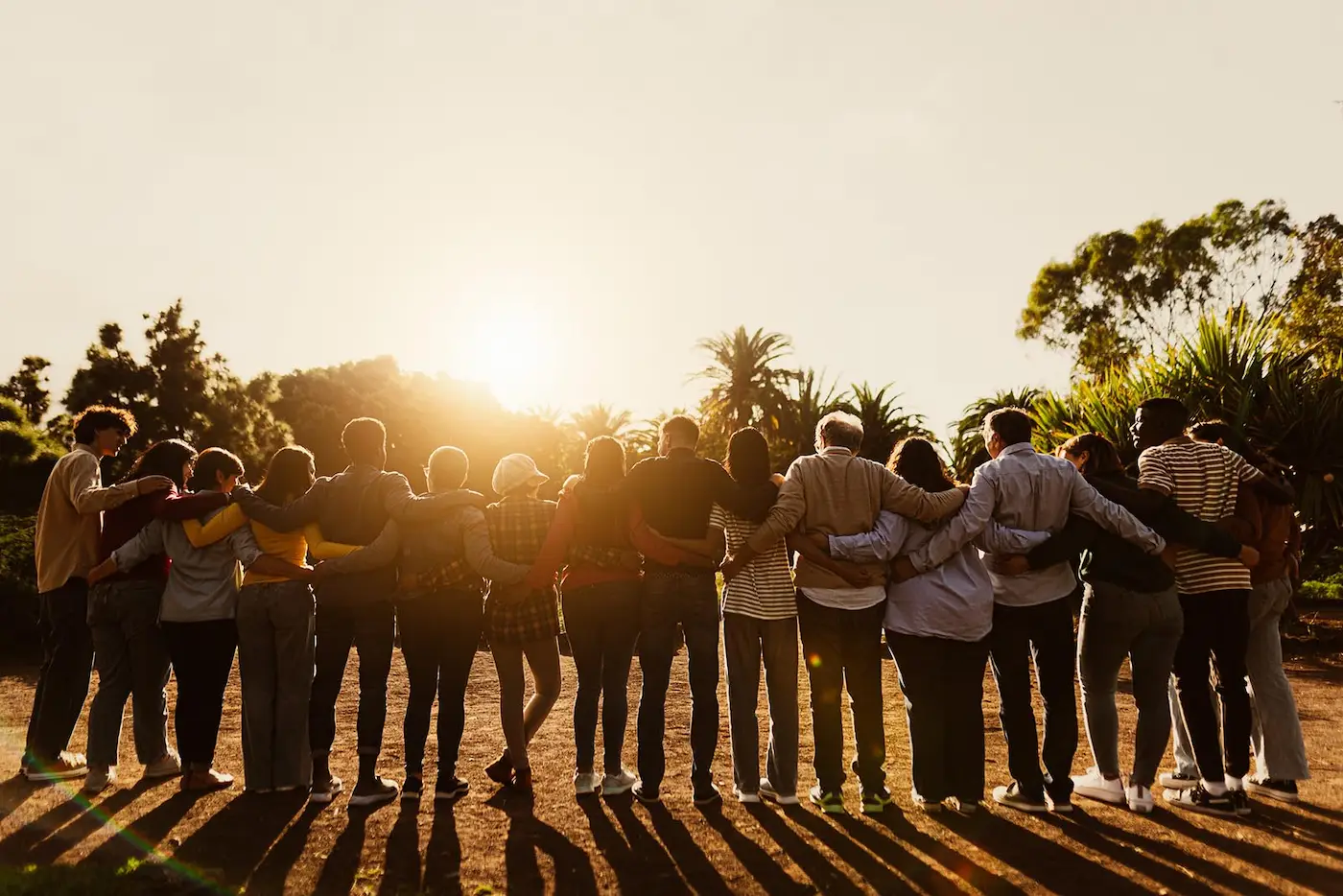 Back view of happy multigenerational people embracing in a public park during sunset